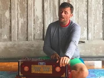 a yoga teacher seated with a harmonium, blending music into meditation practice