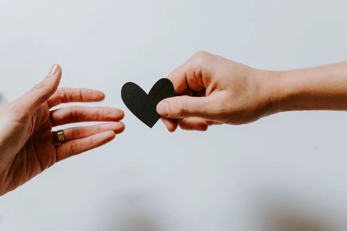 one hand passing a paper heart to an open hand, a symbol of giving back